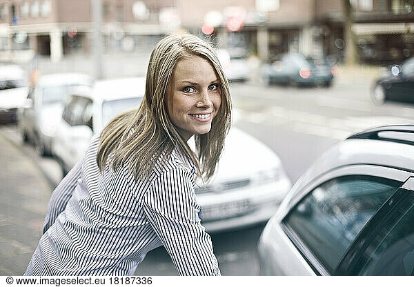 Germany  Duesseldorf  Young woman getting in to car  smiling  portrait