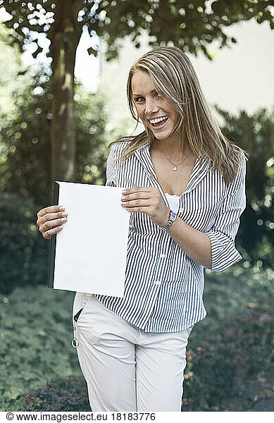 Germany  Duesseldorf  Young woman holding folder  smiling  portrait