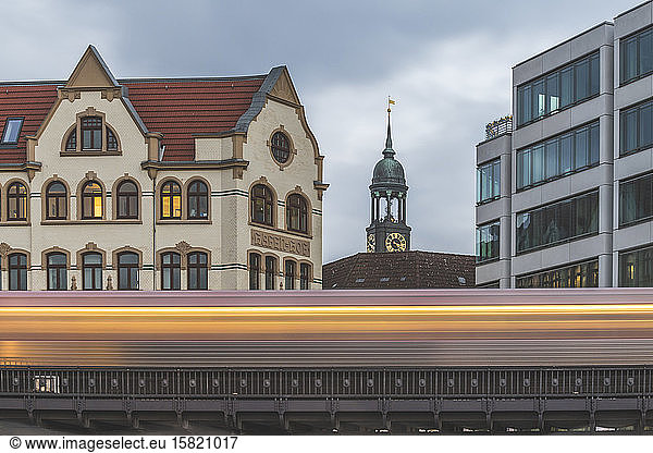 Germany  Hamburg  Blurred motion of elevated train passing residential building with tower of Saint Michaels Church in background