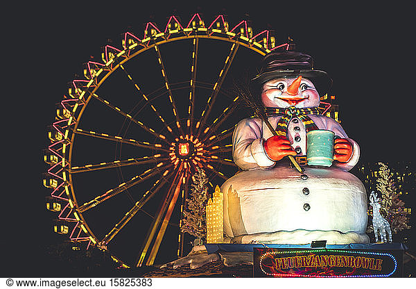 Germany  Hamburg  Low angle view of large snowman sculpture against glowing Ferris wheel at night