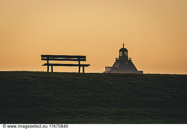 Germany  Hamburg  Silhouette of empty park bench at moody dusk with Great Tower Neuwerk lighthouse in background