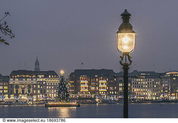Germany  Hamburg  Street light glowing in front of Alster Lake at dusk with Christmas tree in background