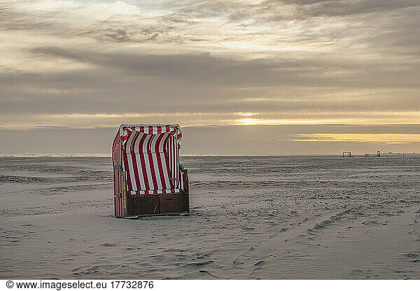 Germany  Lower Saxony  Juist  Hooded beach chair on empty beach at sunset
