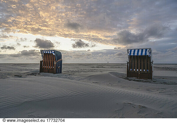 Germany  Lower Saxony  Juist  Hooded beach chairs on empty beach at sunset