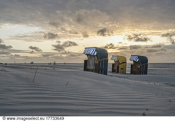 Germany  Lower Saxony  Juist  Hooded beach chairs on empty beach at sunset