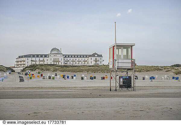 Germany  Lower Saxony  Juist  Lifeguard hut and hooded beach chairs on empty beach with Strandhotel Kurhaus in background