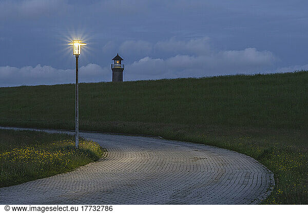 Germany  Lower Saxony  Juist  Street light illuminating paved footpath at dusk with lighthouse in background