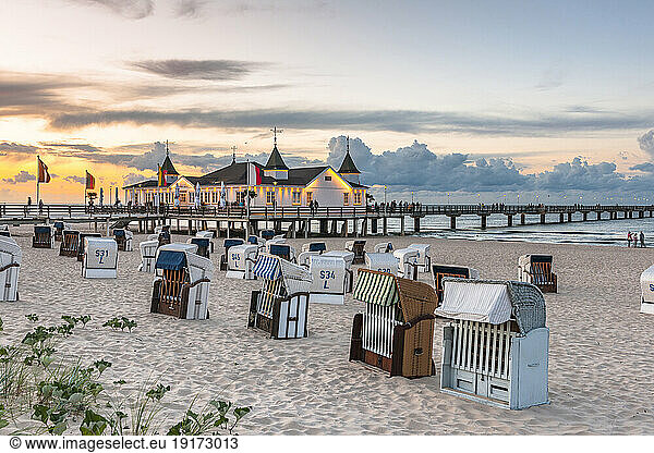 Germany  Mecklenburg-Vorpommern  Ahlbeck  Hooded beach chairs at sunset with pier and bathhouse in background
