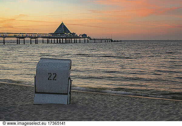 Germany  Mecklenburg-Western Pomerania  Heringsdorf  Hooded beach chair standing on sandy coastal beach at dusk with Heringsdorf Pier in background