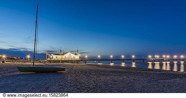 Germany  Mecklenburg-Western Pomerania  Heringsdorf  Sailboat left on sandy coastal beach at dusk with illuminated pier in background