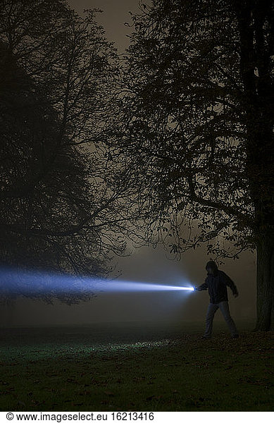 Germany  Munich  Man lighting spooky tree with torch in foggy night