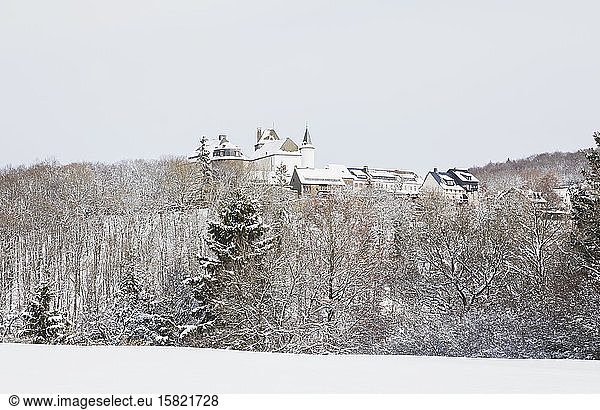 Germany  North Rhine-Westphalia  Hellenthal  Snow-covered forest in front of rural village with Wildenburg Castle in background