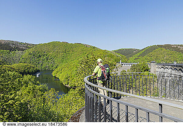 Germany  North Rhine Westphalia  Senior hiker looking toward Rursee lake from viewing platform