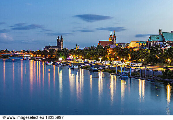 Germany  Saxony-Anhalt  Magdeburg  Boats on bank of Elbe river at dusk with city buildings in background