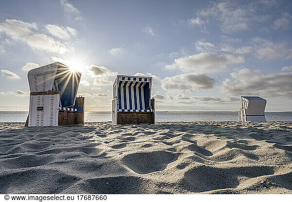 Germany  Schleswig-Holstein  Hornum  Morning sun shining over empty hooded beach chairs standing on sandy beach