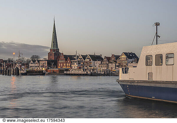 Germany  Schleswig-Holstein  Lubeck  Skyline of Travemunde at dusk with ferry in foreground
