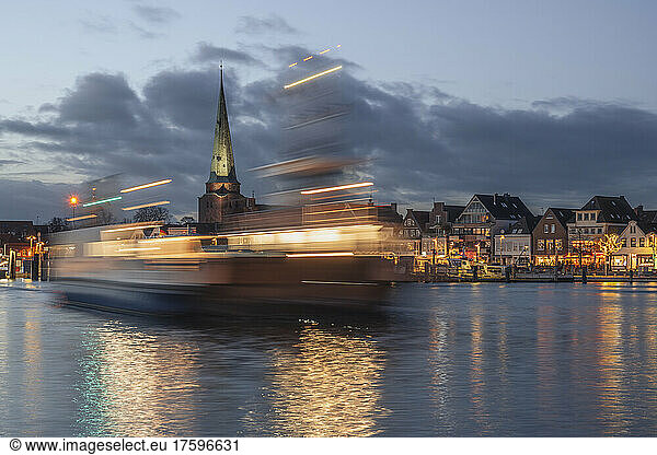 Germany  Schleswig-Holstein  Lubeck  Skyline of Travemunde at dusk with ferry moving in foreground