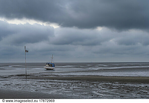 Germany  Schleswig-Holstein  Pellworm  Storm clouds over fishing boat left on beach during low tide