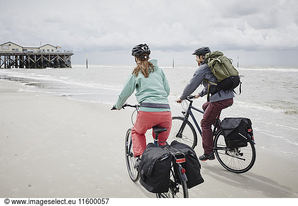Germany  Schleswig-Holstein  St Peter-Ording  couple riding bicycle on the beach