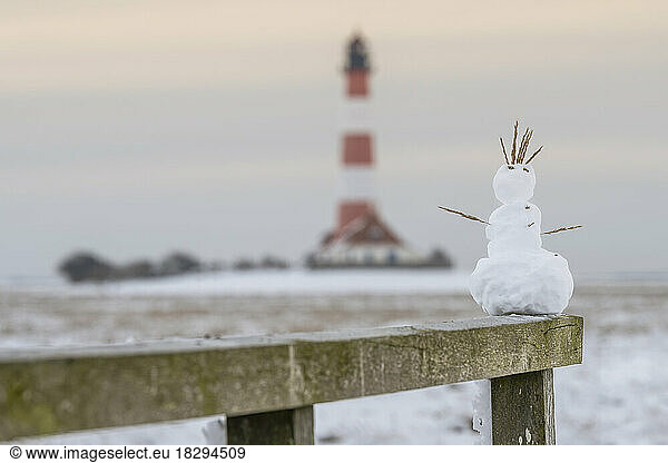 Germany  Schleswig-Holstein  Westerhever  Small snowman on top of wooden fence with Westerheversand Lighthouse in background
