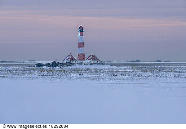 Germany  Schleswig-Holstein  Westerhever  Snow-covered field at dusk with Westerheversand Lighthouse in background