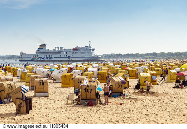 Germany  Travemuende  crowded beach with hooded beach chairs and driving ferry in the background