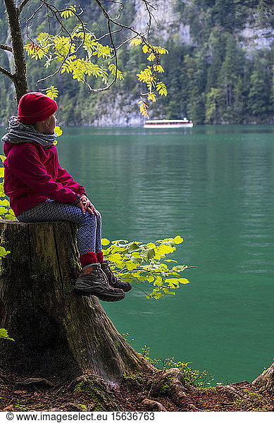 Germany  Upper Bavaria  Girl sitting on tree stump at Lake Keonigssee