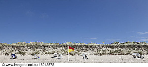 Germany View of empty beach with roofed wicker beach chairs and flag on Sylt island