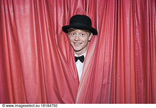 Germany  Young magician behind curtain  smiling
