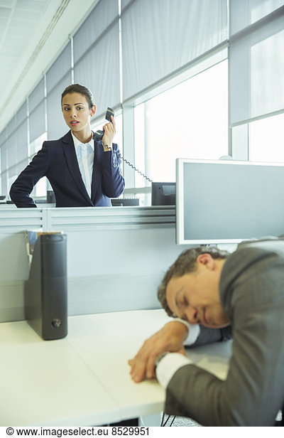 Geschäftsfrau beobachtet schlafenden Geschäftsmann im Büro
