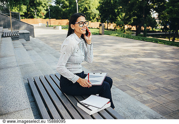 Geschäftsfrau  die anruft und auf einer Parkbank sitzt