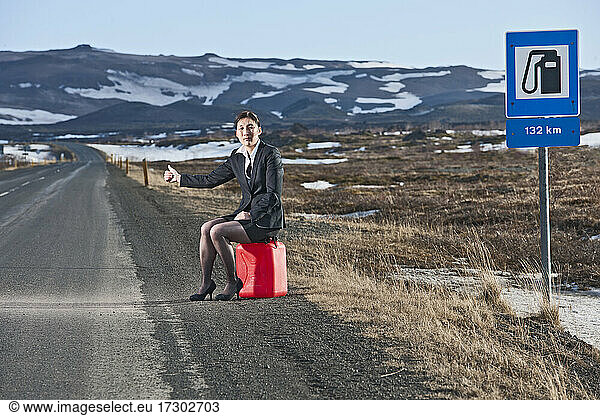 Geschäftsfrau  die auf einem Benzinkanister sitzt und versucht  in Island zu trampen