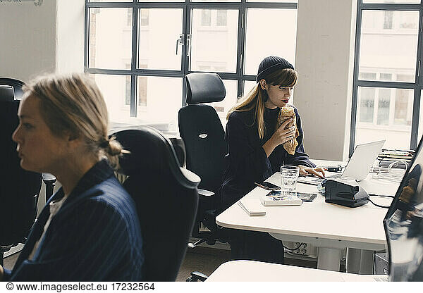 Geschäftsfrau essen Essen während der Arbeit am Laptop im Büro