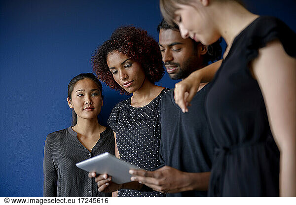 Geschäftsfrau mit Blick auf internationale männliche und weibliche Kollegen  die an einem digitalen Tablet vor blauem Hintergrund arbeiten