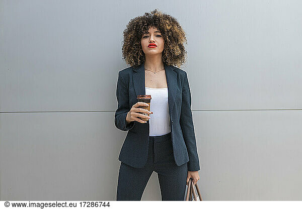 Geschäftsfrau mit Handtasche bei einem Kaffee vor einer grauen Wand
