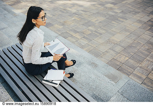 Geschäftsfrau mit Klemmbrett auf einer Parkbank sitzend