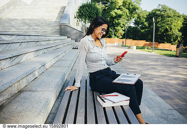 Geschäftsfrau mit Smartphone auf einer Parkbank sitzend