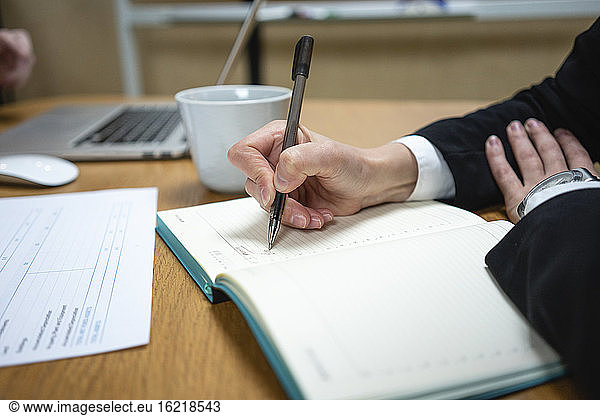 Geschäftsfrau schreibt in Tagebuch an beleuchtetem Schreibtisch