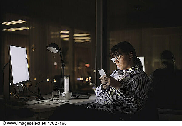 Geschäftsfrau Textnachrichten auf Smartphone sitzend am Arbeitsplatz