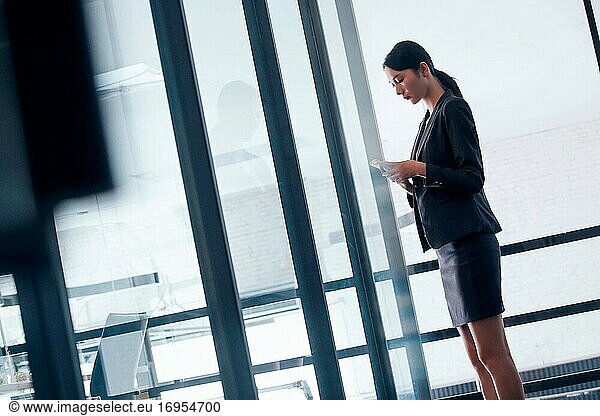 Geschäftsfrau vor dem Fenster stehend  um ein Mobiltelefon zu sehen