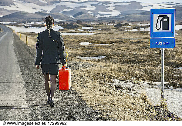 Geschäftsfrau zu Fuß mit Benzinkanister auf leerer Straße in Island