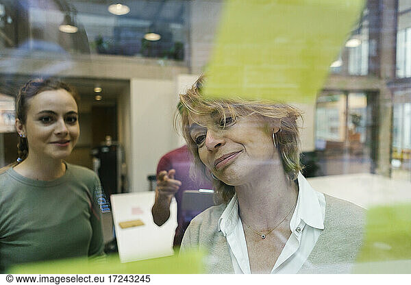 Geschäftsfrauen mit Blick auf Haftnotizen auf Glas im Büro durch Glas gesehen