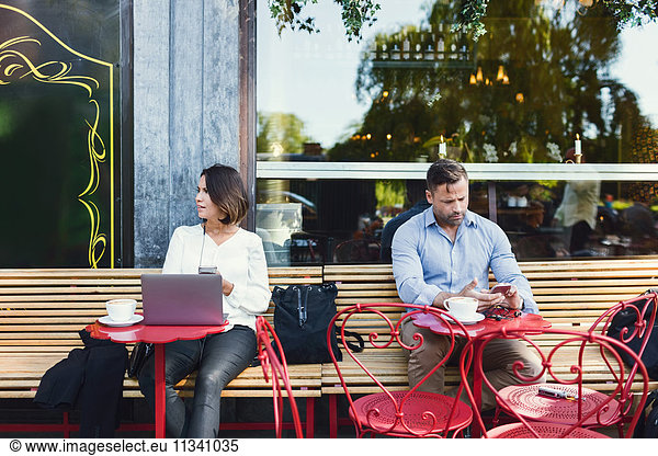 Geschäftsleute  die Technologien im Straßencafé nutzen.