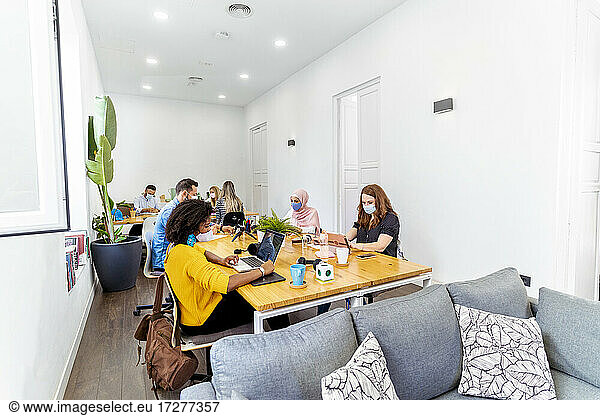 Geschäftsleute mit Gesichtsmaske  die in sozialer Distanz sitzen  während sie im Büro sitzen