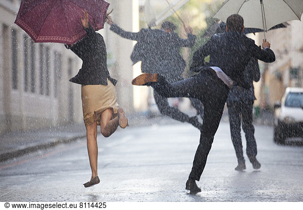 Geschäftsleute mit Regenschirmen tanzen im Regen