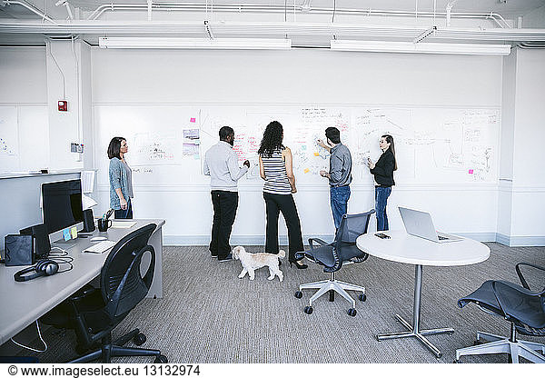Geschäftsleute schreiben Notizen auf weißer Tafel und diskutieren im Büro