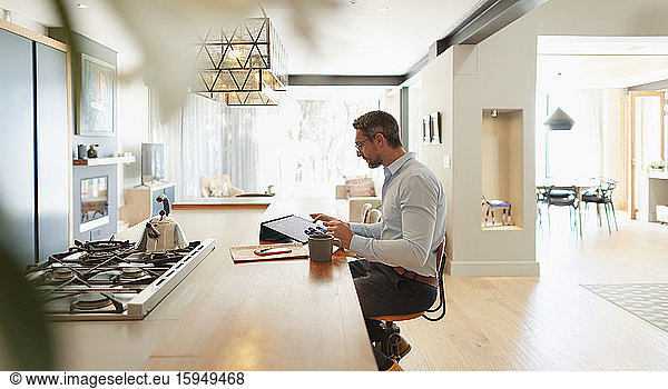 Geschäftsmann am digitalen Tablet der von zu Hause aus in einer modernen Küche arbeitet