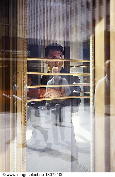 Geschäftsmann  der durch ein Glasfenster mit Spiegelung von Menschen wegsieht