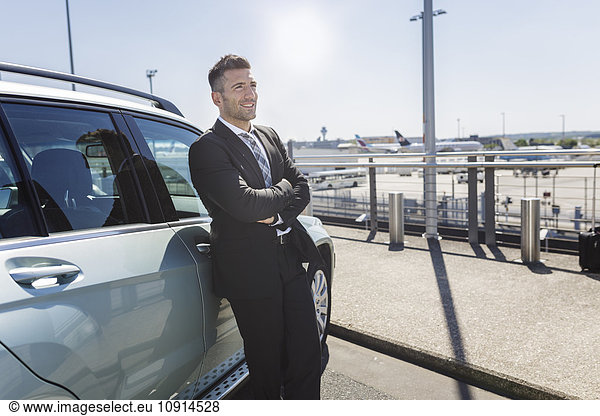Geschäftsmann  der sich am Flughafen gegen das Auto lehnt.