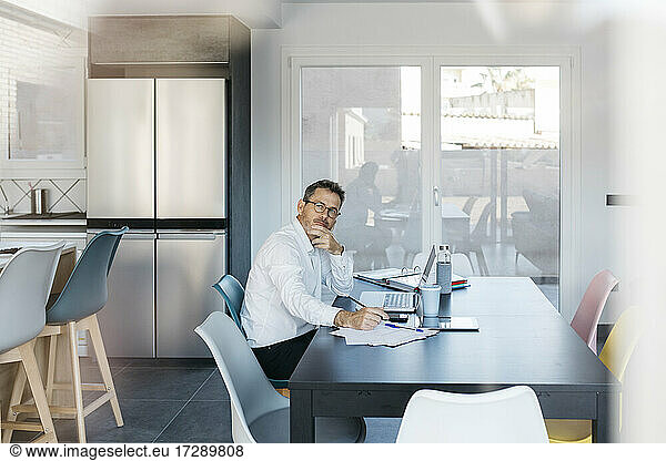 Geschäftsmann  der wegschaut  während er am Tisch im Heimbüro sitzt